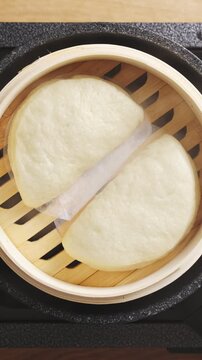 Chef&rsquo;s hand opens bamboo lid, showing hot bao buns. Bao buns steam without frying, keeping texture soft and fluffy. Fill bao buns with vegetables, tofu, chicken or seafood for light Asian meal.