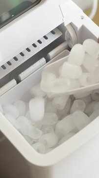 Vertical video of taking fresh ice cubes from home ice maker machine