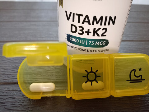 Moscow, Russia - 07.22.2026: A medication organizer with an open compartment containing a vitamin D capsule in front of a supplement jar labeled "Vitamin D3 Plus K2" in English - horizontal photo, clo