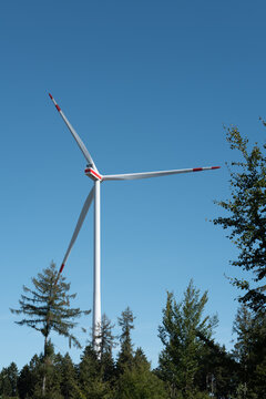 Wind turbine stands tall against a clear blue sky with trees surrounding it in a rural area