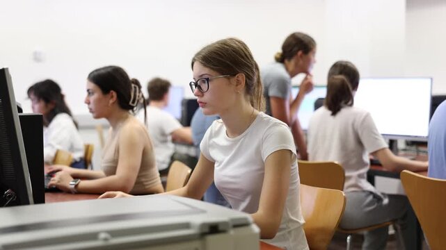Interested young female student with glasses working on computer in university library, looking for necessary information on Internet 