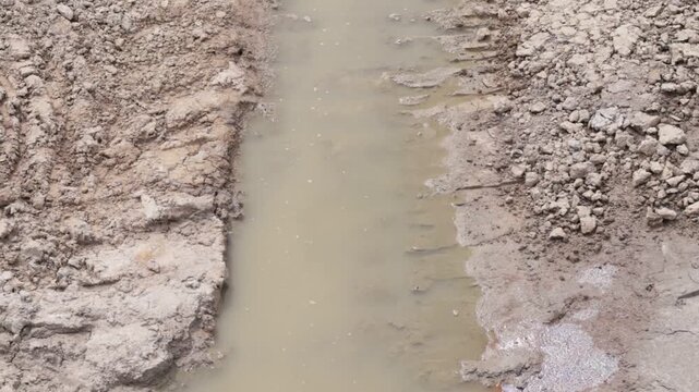 Rough, fractured soil frames a narrow channel of murky liquid; the scene conveys exposed subsurface and damp, unfinished work
