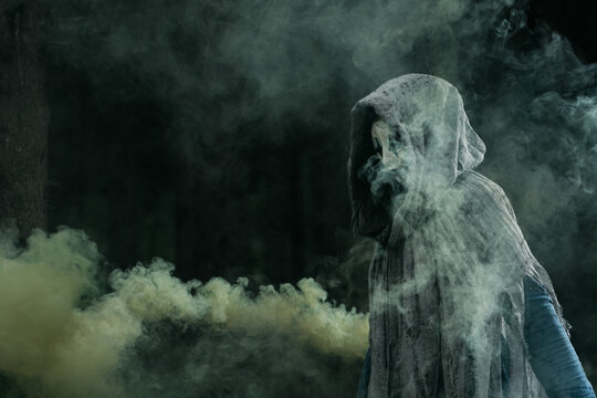 Spooky and scary Halloween themed image in a dark forest with smoke and an eerie woman with a mask. .