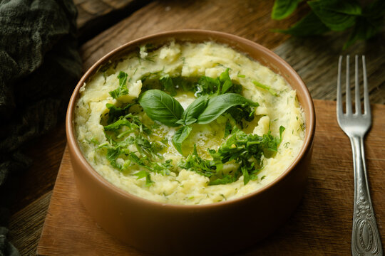 Bowl of mashed potatoes garnished with fresh herbs on rustic wooden table. Thanksgiving meal.