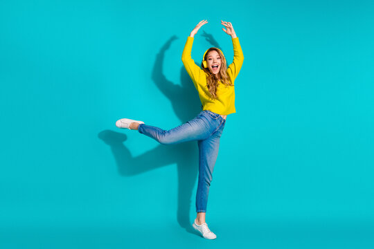 Young woman dancing in a bright yellow sweater with jeans and white sneakers against a blue background lifestyle fashion advertising and playful promotional campaigns
