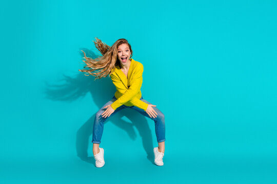Happy young woman in a yellow sweater on blue background smiling and jumping for fashion lifestyle image