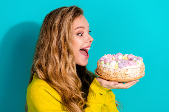 Young woman with blonde hair holds a colorful cake against a blue background celebrating a sweet moment