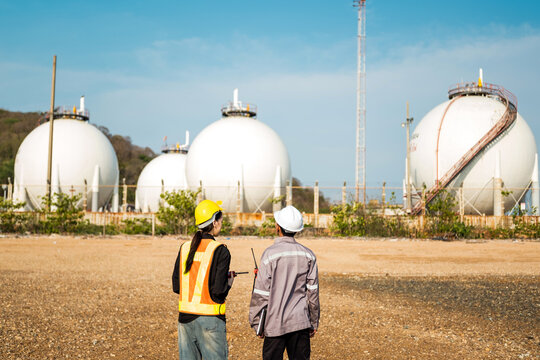 Two engineers in safety gear inspect spherical gas storage tanks at an industrial plant under a clear sky