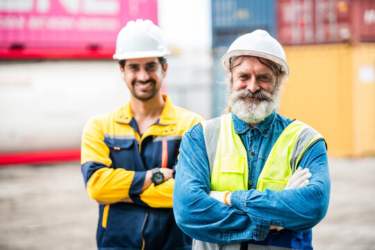 Two industrial workers in hard hats and safety gear stand smiling at a container yard, conveying teamwork and confidence in a shipping and logistics environment.