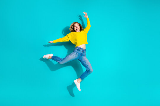Joyful young woman jumps in a bright yellow sweater against a blue background for a vibrant fashion lifestyle stock photo