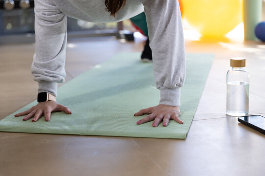 Female wearing gray sweatshirt performing exercise on green yoga mat in gym with water bottle phone