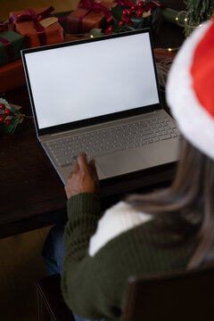 African American woman in Santa hat sitting at table using laptop with wrapped gifts, copy space