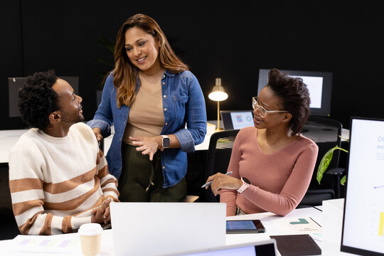 African American colleagues standing and talking at desk, pointing at tablet near laptop and coffee