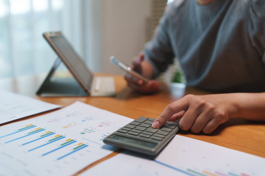 Close-up of reviewing expenses with a calculator, smartphone, and tablet while analyzing financial reports, budgeting, and business performance for accurate planning.
