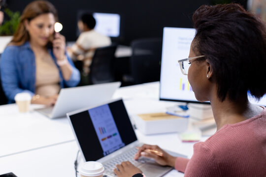 Diverse team working in office, African-American woman at right typing on laptop, copy space