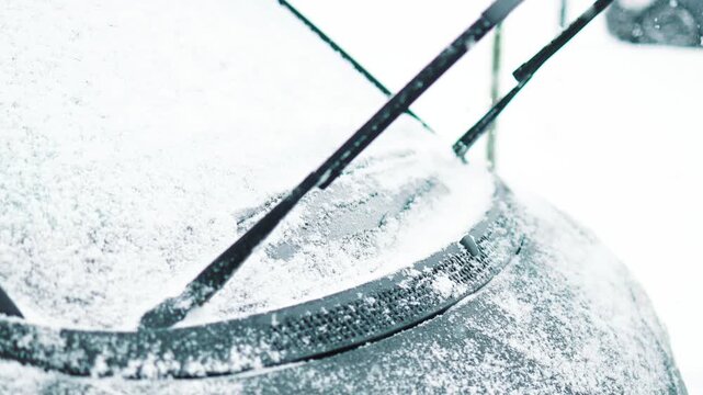 Close-up of a person clearing fresh white snow off an automobile front window and wipers after blizzard. Winter vehicle maintenance, automotive care, and freezing weather concept.