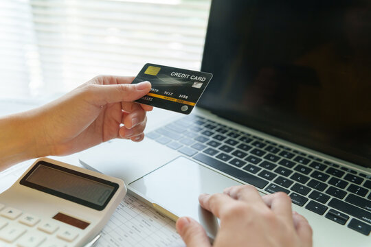 Woman using a credit card, calculator and laptop to review expenses and make secure online payments, representing digital banking and personal finance management.