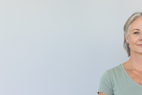 Senior woman standing in studio facing forward against gray wall wearing green shirt, copy space