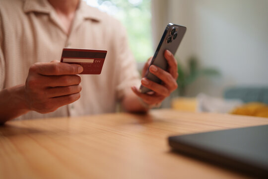 Man holding a payment card and smartphone at home for online registration and identity verification, representing secure authentication, mobile banking, digital payment and personal data.