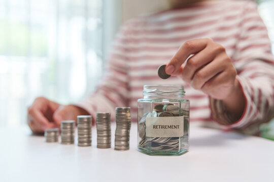 Female hand Adding coins into a retirement fund jar with growing stacks represents disciplined saving, long-term investing and future financial security.