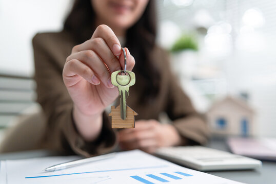 Real estate agent holding a house key with home symbol above financial paperwork, representing property purchase, mortgage loan, home ownership, investment and housing transactions.