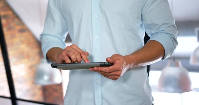 Asian man in blue shirt lifting tablet, tapping, swiping, rotating grip and presenting in office