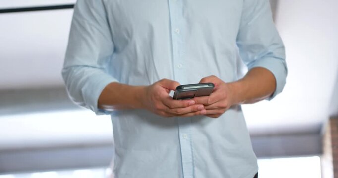 Camera pulling back Asian man holding smartphone blue-shirt scrolling thumbs reading text at window