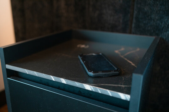 Close-up of a mobile phone screen up on a black luxury nightstand in bedroom. Concept of wireless technology, digital connectivity, morning screen time checking, and minimalist interior design.