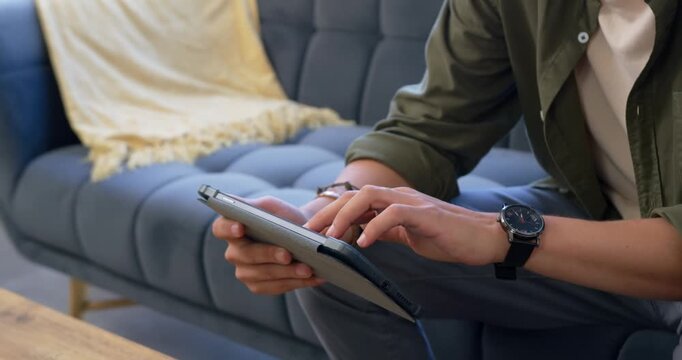 Adult male sitting on tufted sofa, left hand supporting tablet with cable, tapping to read