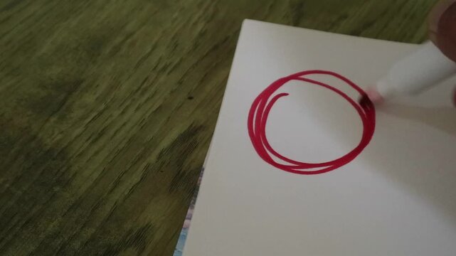A person drawing a red circle on white paper with a marker.