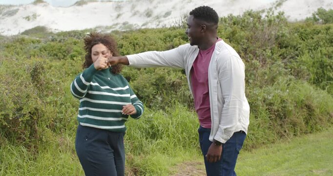 African American couple woman offering hand man guiding spin sharing love on dune path striped top
