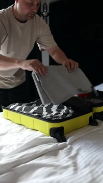 Close-up of a male traveler trying to zip a packed luggage bag filled with clothes in hotel bedroom. Travel preparation, luggage packing, and vacation departure concept.