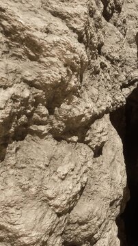 A close up view of a rock formation in a canyon. The sunlight hits the surface, showing different textures. The colors appear neutral with rugged details creating an interesting landscape.