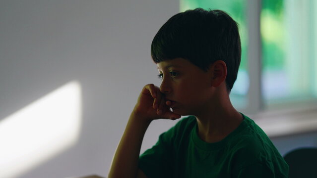 Pensive thoughtful young boy resting chin on hand at home, deeply contemplating a problem, expressing curiosity, concentration, emotional reflection