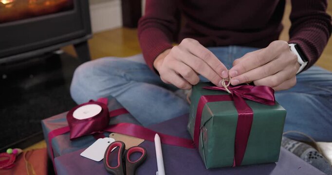 African American man in living room choosing green gift tightening ribbon tying twine labeling gift