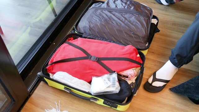 High angle of a male traveler organizing garments inside an open luggage bag near a doorway. Concept of travel preparation, packing for a trip, and vacation departure.