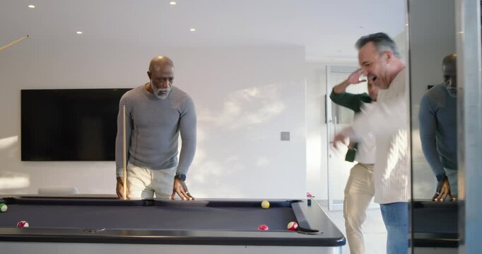 Diverse men watching senior African-American man tapping cue to win, sinking ball, cheering in den
