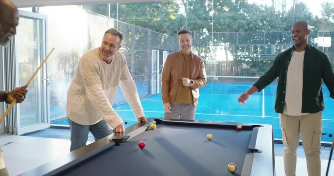 Male friends playing on blue-felt pool table in game room, watching leftmost man lining up shot