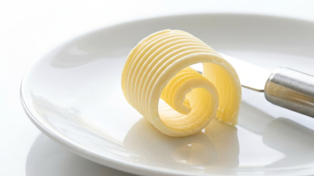 Single fresh yellow butter curl with delicate ridged texture served on a white plate with a knife