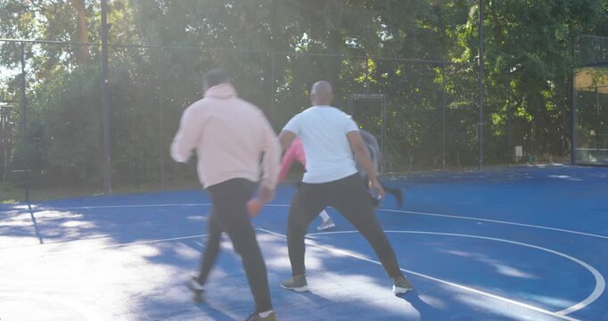 Diverse men dribbling baseline on blue court, drawing hoodies and finishing layup to score at hoop