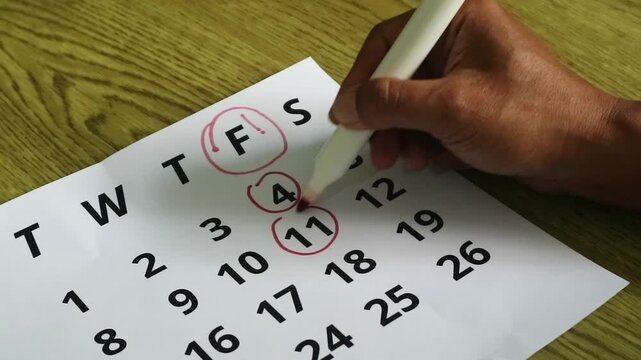 Person marking dates on a paper calendar with a red marker pen.
