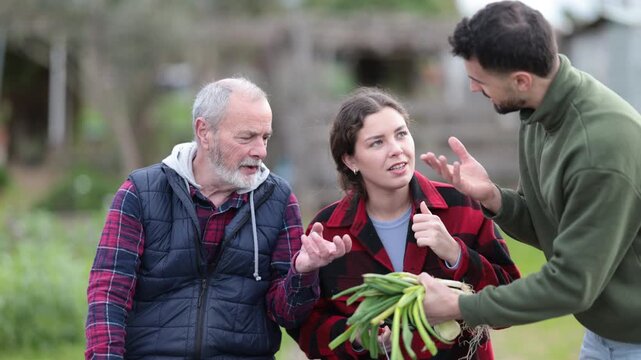 Couple young man and woman have friendly conversation with eldery man while harvesting green onions in garden 