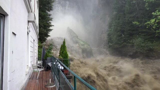 Close-up of a swollen waterfall next to a house due to heavy flooding. Serious consequences of climate change.