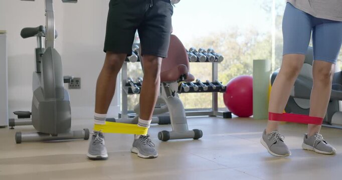 Bands around ankles, African American pair doing lateral steps in home gym for lower-body strength