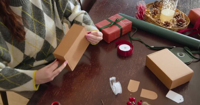 Woman argyle pulling red ribbon tying bow on kraft box at wooden-table wrapping gifts, copy space