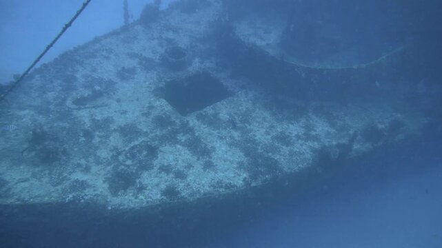 Underwater pan follows the broad encrusted forward section of C-56 Juan Escutia shipwreck through blue water in Puerto Morelos, Quintana Roo, Mexico.