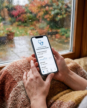 Hands holding smartphone with mobile health care app on screen near rain window autumn background