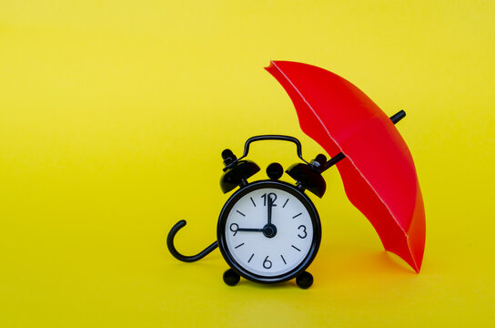 Alarm clock sheltered under a red umbrella illustrating risk protection, insurance planning and security management.