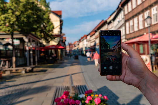 Close up of hand holding smartphone taking photo of historic timber-framed houses in Wernigerode Old Town, travel photography and mobile app concept
