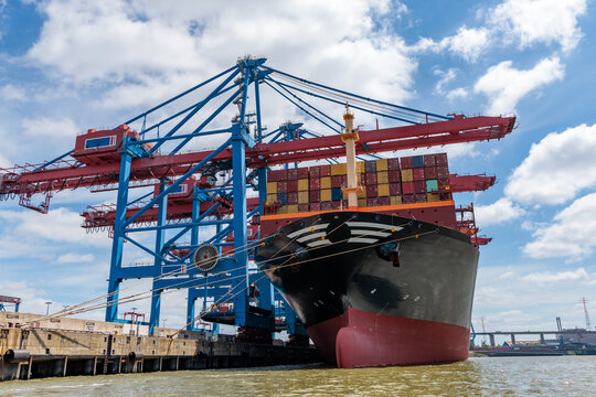 Large container ship docked at container terminal under gantry cranes on sunny day in Port of Hamburg, global logistics and maritime shipping concept